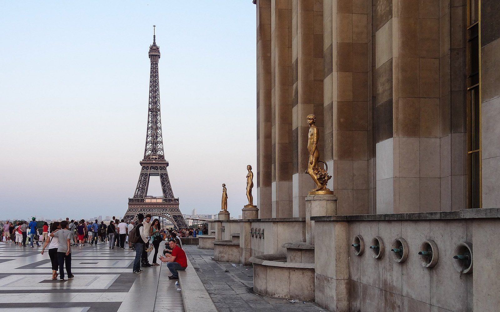 Gilded statues line the Trocadéro terrace overlooking the Eiffel Tower and crowds below