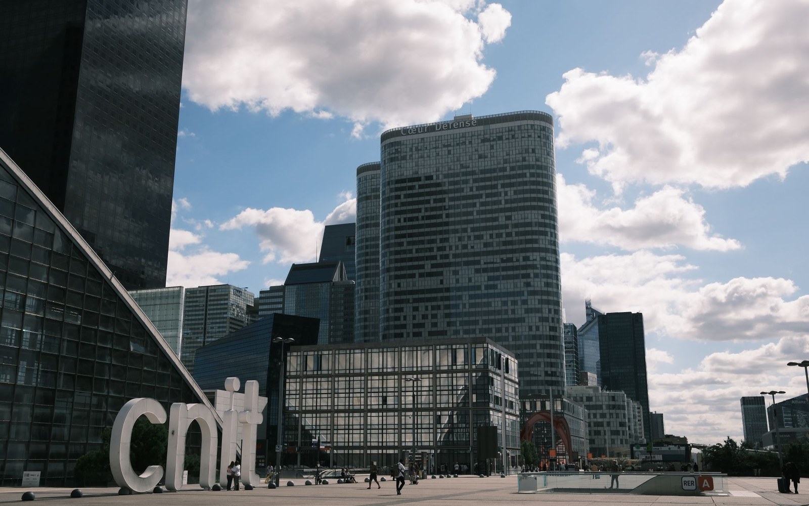Skyscrapers rise behind the CNIT building's plaza sign at La Défense under a cloudy sky