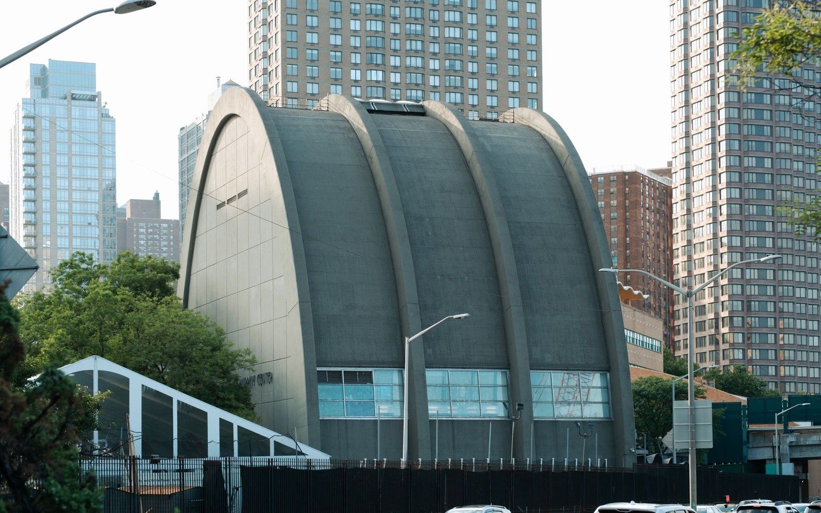 Curved concrete arched building with vaulted roof surrounded by high-rise apartment towers