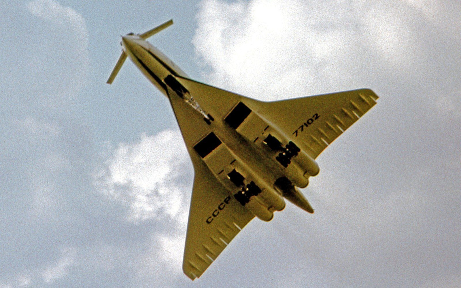 Underside view of a swept-wing Tupolev jet banking against a cloudy sky